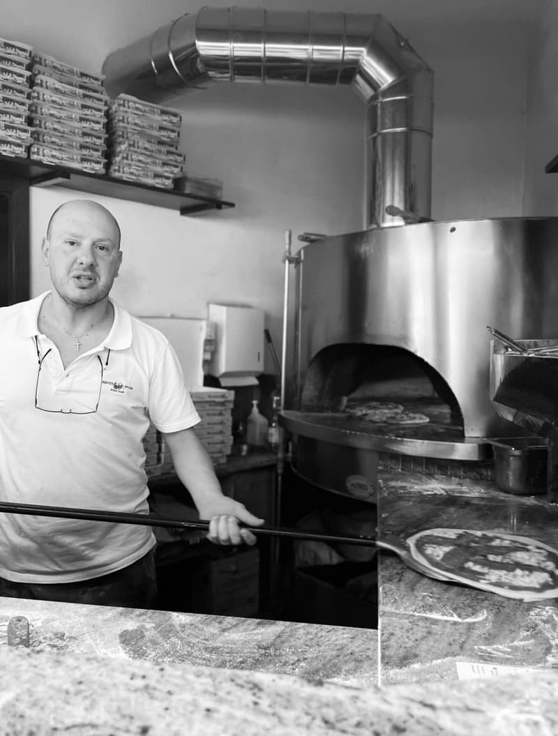 Pizzaiolo schiebt eine Pizza mit der Schaufel in den Holzofen